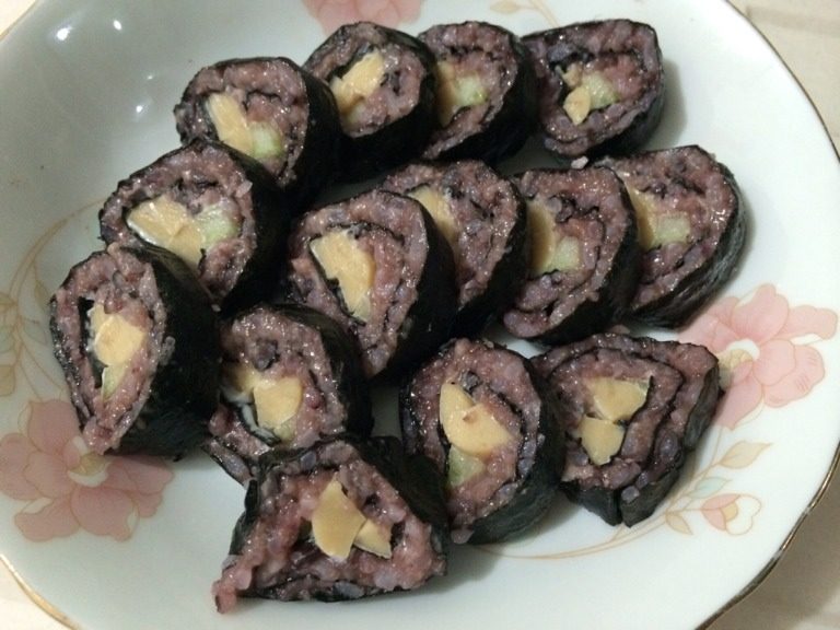 紫米寿司,将卷好的寿司,用刀切成厚片装盘即可,