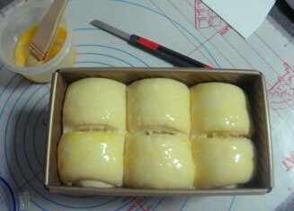 椰蓉吐司,用刀在表面割一条开口,表面刷蛋液,入烤箱底层烘焙