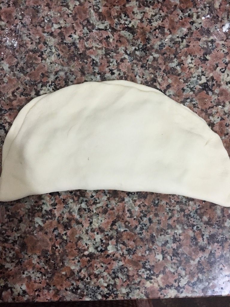 葱花猪肉馅饼,取一团面团,用擀面杖擀成薄块状,把做好的馅平铺在半张面饼上面,再把另外半张面饼捏紧。如图