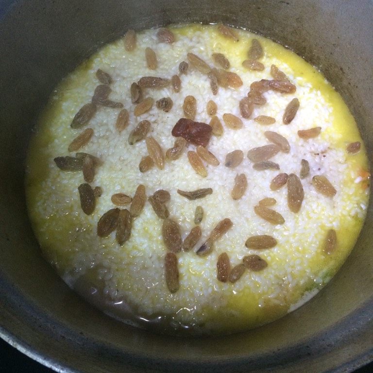 羊肉手抓饭,如图将下入的大米用铲子稍微抹平,看水量少的话可稍微再添加一些,标准以电饭煲蒸饭的用水量为依据,撒上葡萄干