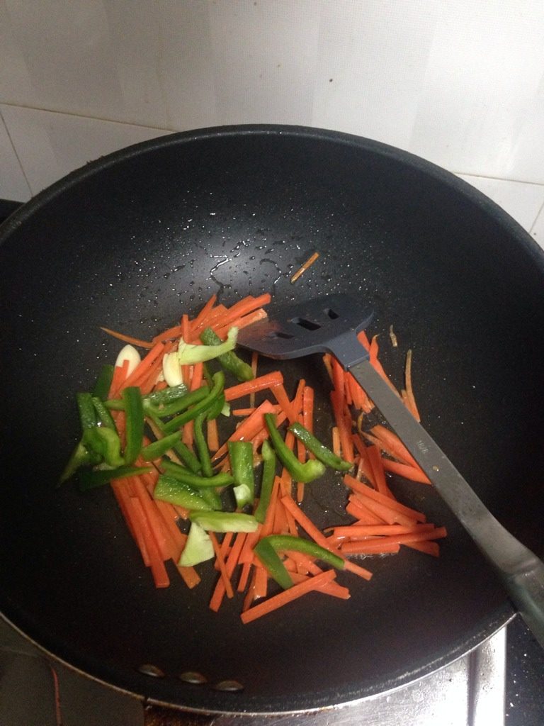 青椒萝卜炒豆干肉丝,如图洗锅重新起锅,放入蒜头、胡萝卜、青椒。炒至软身
