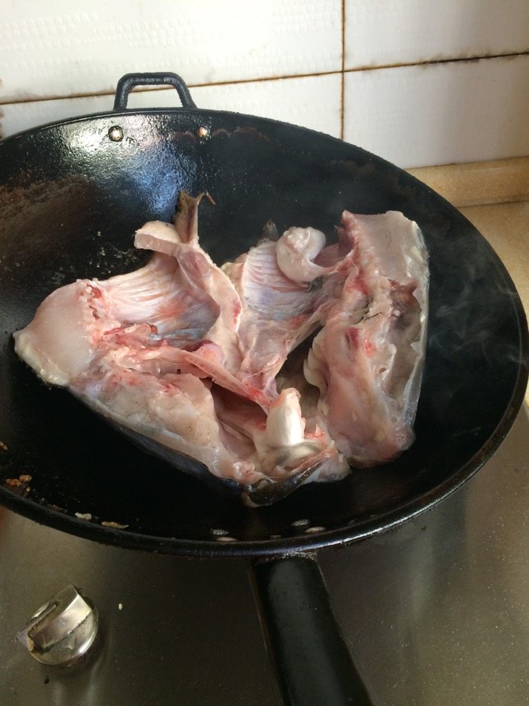 鱼头火锅,食用油烧热后,放入劈开的鱼头中火慢煎