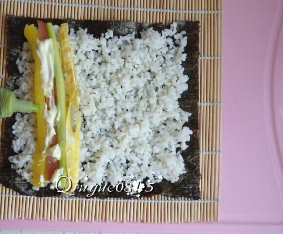 基础寿司,当然也可以这样不铺保鲜膜,米饭尽量不要压实。然后在靠近自己这一端的米饭上放上火腿肠、黄瓜、大根条、沙拉酱、青芥辣。