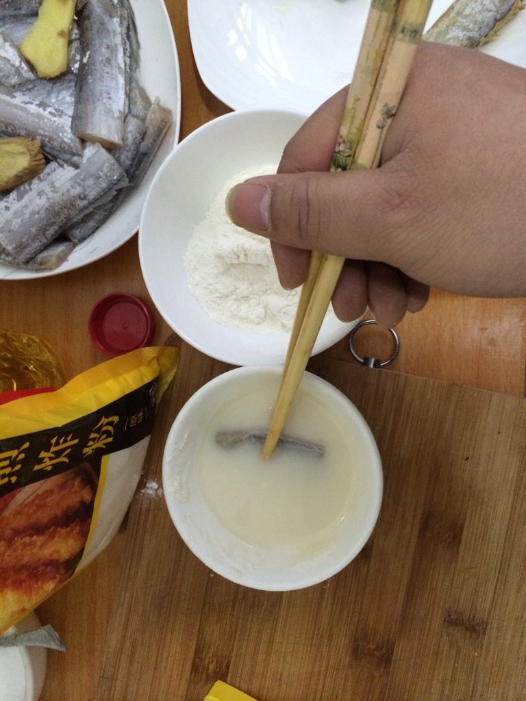 干烧带鱼,如图裹粉时,一碗加水调稀,一碗干粉。先把鱼放入稀释的粉中裹上一层粉液然后再放入干粉碗中裹上一层干粉,这样油炸时不会粘锅
