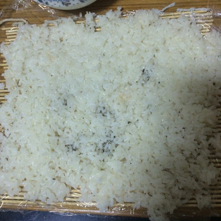 泡菜反卷寿司,如图在寿司帘上铺上一层保鲜膜，最好刷点儿油，均匀的铺上糯米饭