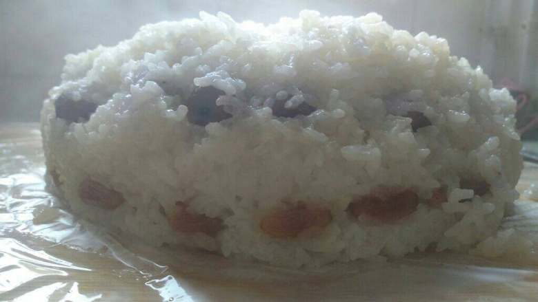 电饭锅菜谱 红枣糯米饭,煮熟后在案板上铺保鲜膜,把饭倒扣过来装盘就好了。因为时间晚了急着吃,所以有很多热气拍不清楚,不急的话等凉透再倒是很整齐的。