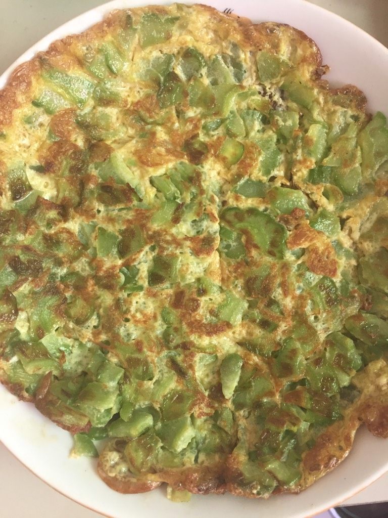 苦瓜煎蛋,如图锅里热油时把搅拌好的苦瓜一圈圈的倒入，一面煎至金黄在翻别一面至金黄即可。