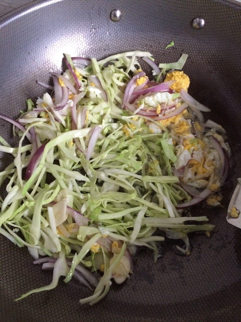 炒饼,如图待鸡蛋六成熟下入洋葱丝,翻炒,卷心菜和蒜片下入翻炒均匀,淋入少许海鲜酱油