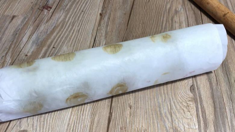 抹茶红豆蛋糕卷,借用擀面杖卷起油纸,将蛋糕压卷起来,边卷边压,卷好后静置片刻定型