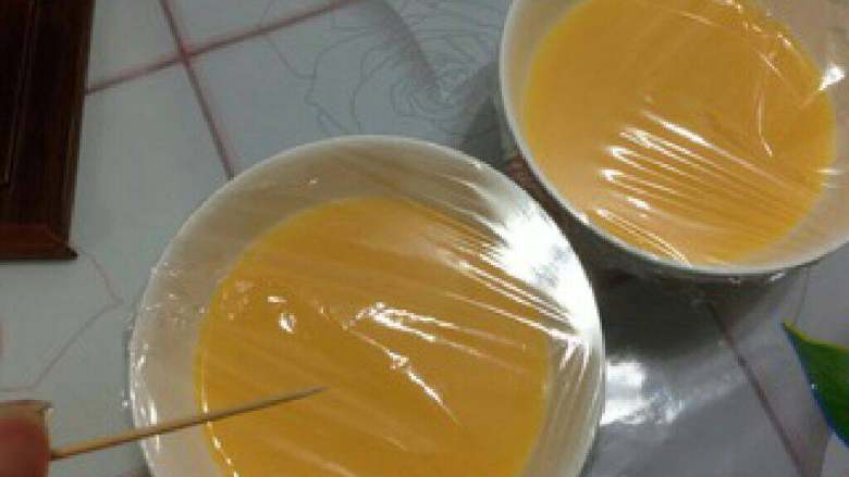 【秋葵鲍鱼蒸鸡蛋羹】,倒入2个碗中,盖上保鲜膜,用牙签刺几个小孔透气。