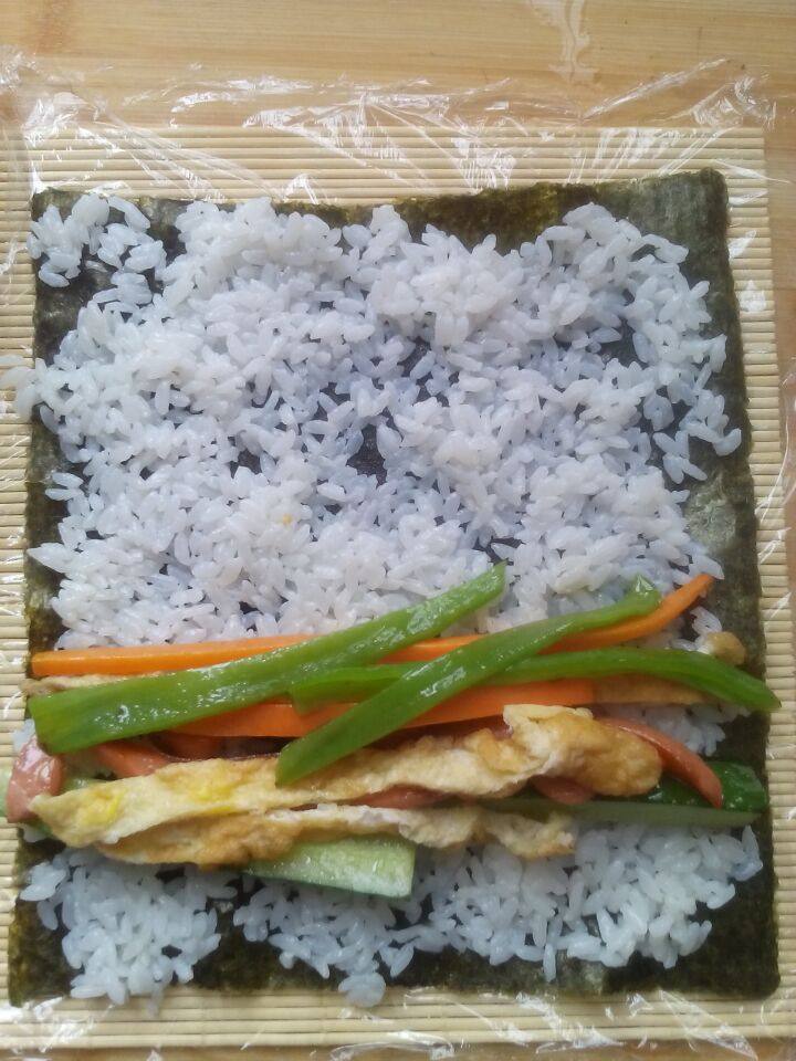 紫菜包饭,竹帘上放上保鲜膜,放上紫菜, 平铺一成米饭, 在摆好菜。