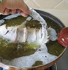糖醋黄鱼,慢慢的把鱼身子放进油锅里,一只手提着鱼尾巴,另一只手拿着勺子要将鱼头抬起
