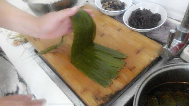 豆沙蜜豆粽子,把八片粽叶平铺在菜板上不能有缝隙,用手淋点水在粽叶上,然后折一下如有图