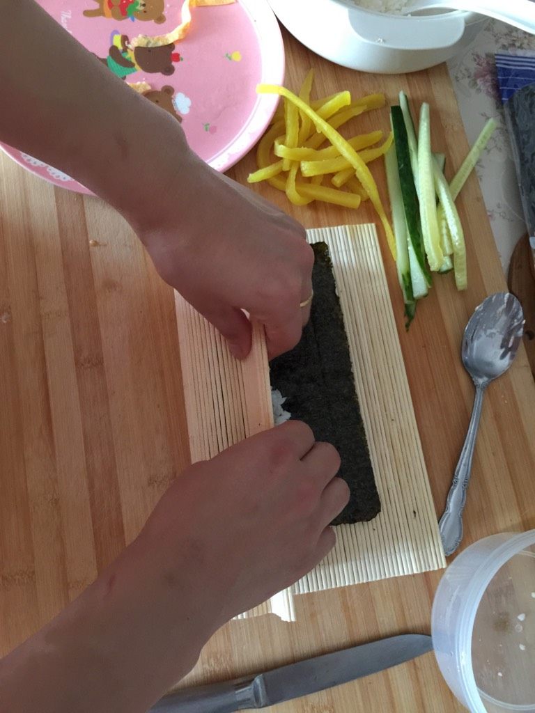 紫菜包饭,手托竹帘卷，按压着卷，卷成一条卷