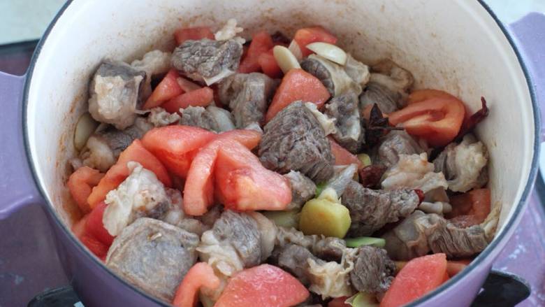 红焖牛肉煲,加入葱姜蒜、八角、桂皮、红干椒和冰糖炒出香味,接着放入番茄块翻炒均匀。