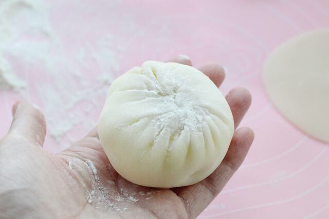 草莓雪媚娘,拎起边缘的饼皮慢慢收口,将奶油和草莓包裹起来,收口处撒熟糯米粉防粘。